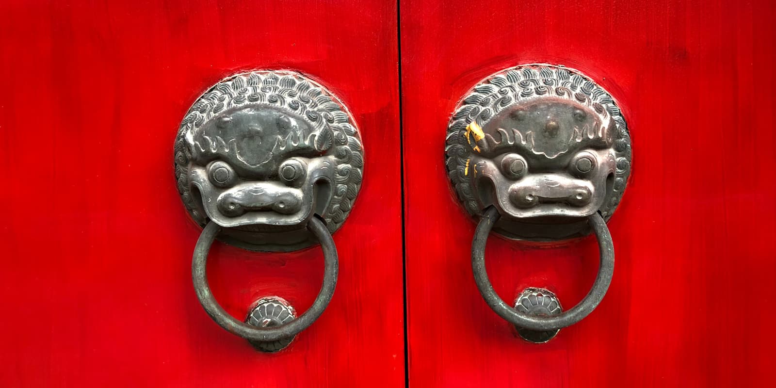 Datenschutz in China: Nahaufnahme einer verschlossenen, roten Türe mit zwei alten, chinesischen Türknöpfen